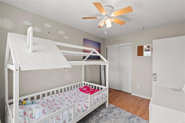 bedroom featuring a closet, a textured ceiling, baseboards, wood finished floors, and a ceiling fan