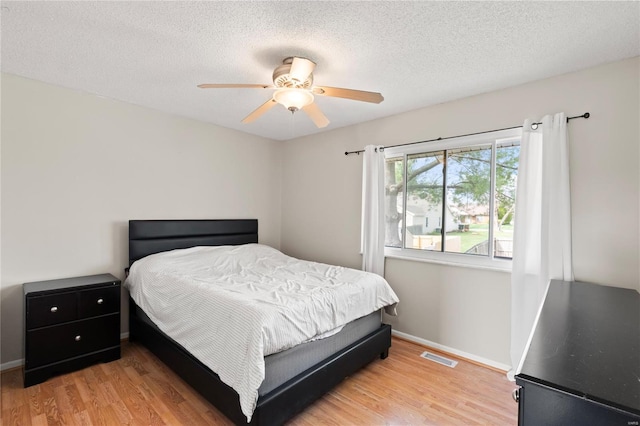 bedroom featuring visible vents, baseboards, light wood finished floors, and a textured ceiling