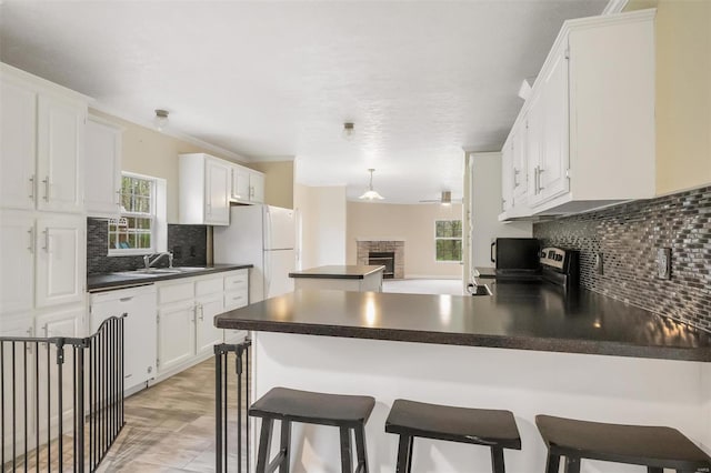 kitchen featuring a peninsula, a wealth of natural light, dark countertops, freestanding refrigerator, and dishwasher