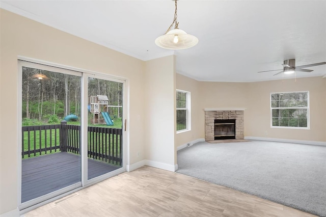 unfurnished living room featuring carpet, a stone fireplace, visible vents, baseboards, and ceiling fan