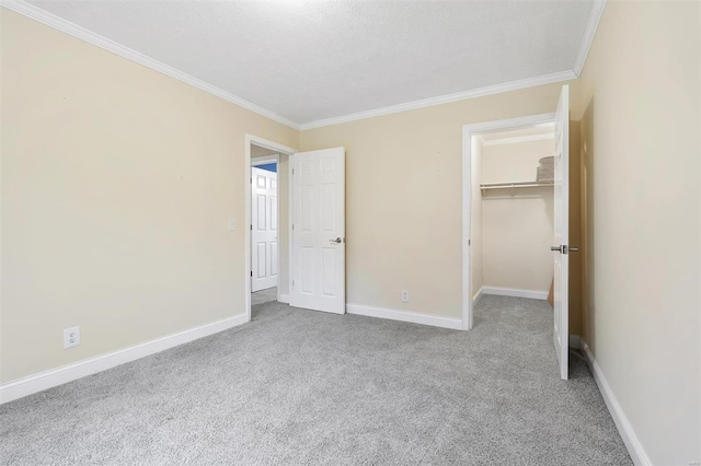 unfurnished bedroom featuring a walk in closet, carpet floors, crown molding, and baseboards