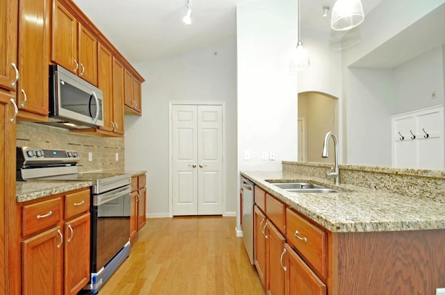 kitchen with brown cabinets, stainless steel appliances, backsplash, a sink, and light wood-type flooring