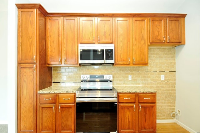 kitchen with light stone counters, brown cabinets, stainless steel appliances, backsplash, and baseboards