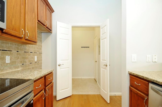 kitchen with brown cabinets, light stone counters, dishwasher, decorative backsplash, and light wood-style flooring
