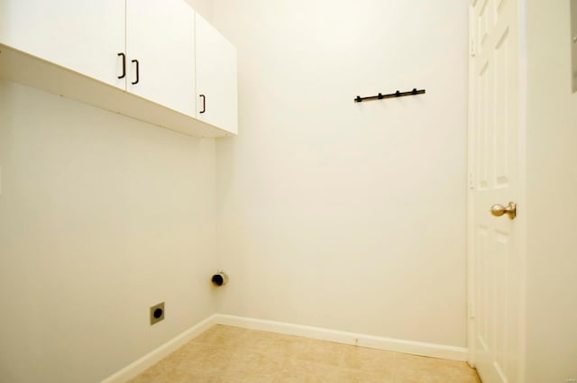 clothes washing area with electric dryer hookup, cabinet space, light tile patterned flooring, and baseboards