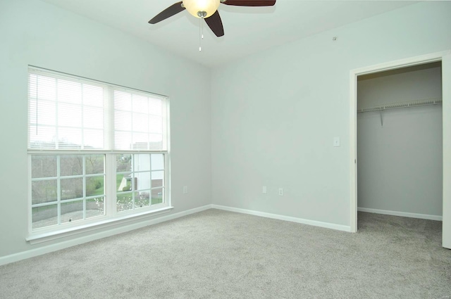 unfurnished bedroom with a closet, a spacious closet, ceiling fan, carpet floors, and baseboards