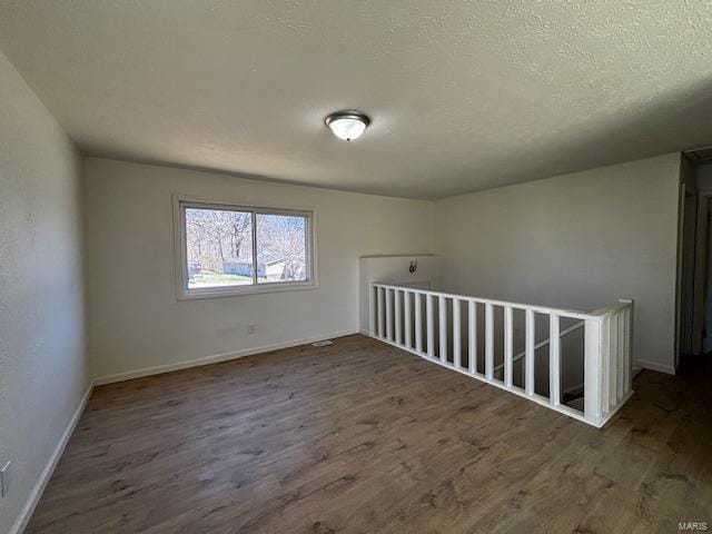 empty room featuring baseboards, a textured ceiling, and wood finished floors