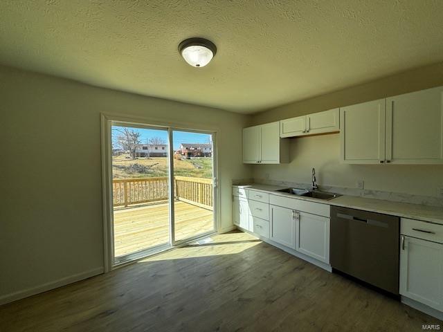 kitchen with a sink, stainless steel dishwasher, wood finished floors, white cabinets, and light countertops