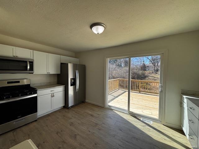 kitchen featuring stainless steel appliances, a textured ceiling, wood finished floors, and white cabinetry