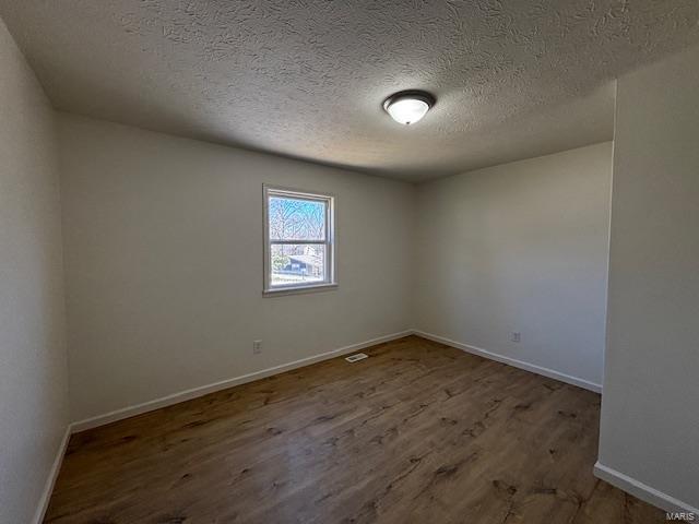 unfurnished room featuring visible vents, wood finished floors, baseboards, and a textured ceiling