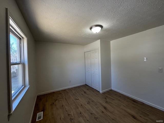unfurnished bedroom featuring wood finished floors, visible vents, baseboards, a closet, and a textured ceiling
