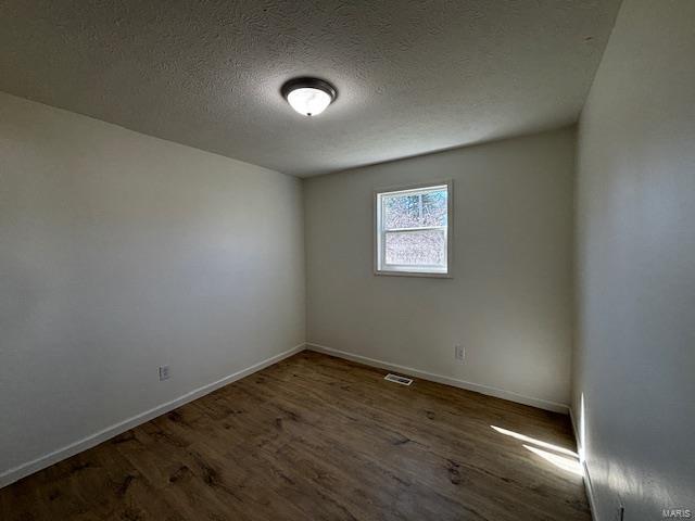 empty room featuring visible vents, baseboards, a textured ceiling, and wood finished floors
