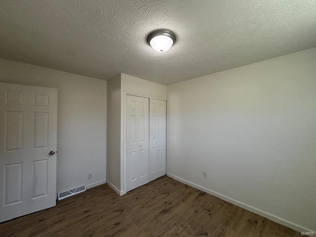 unfurnished bedroom with wood finished floors, visible vents, a closet, and baseboards