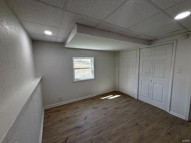 interior space featuring a paneled ceiling, baseboards, and wood finished floors