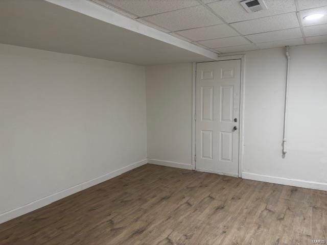 finished below grade area featuring a paneled ceiling, visible vents, baseboards, and wood finished floors