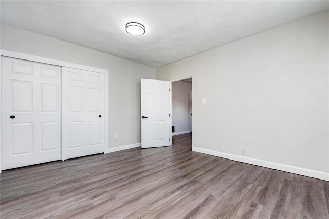 unfurnished bedroom featuring wood finished floors, a closet, and baseboards