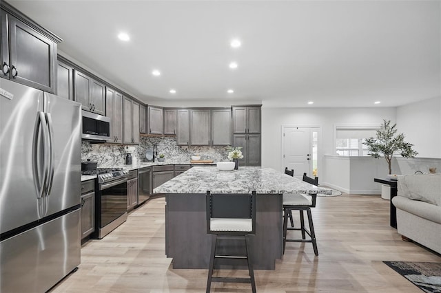 kitchen with backsplash, light stone countertops, a kitchen bar, appliances with stainless steel finishes, and a center island