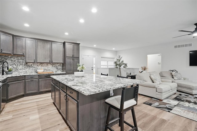 kitchen featuring light stone counters, light wood finished floors, a breakfast bar area, open floor plan, and visible vents