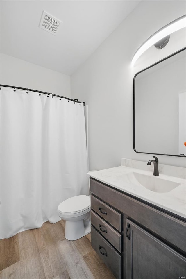 bathroom featuring a shower with curtain, vanity, toilet, visible vents, and wood finished floors