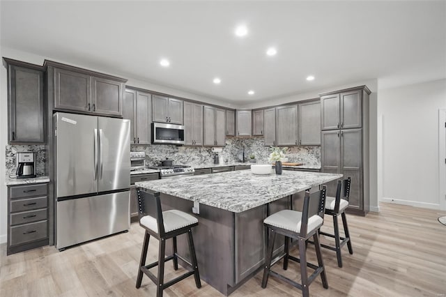kitchen with a kitchen bar, tasteful backsplash, a center island, light wood-style floors, and appliances with stainless steel finishes