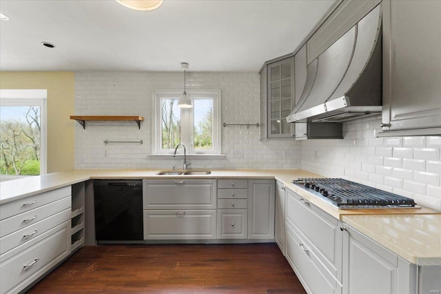 kitchen featuring wall chimney range hood, open shelves, dark wood-type flooring, dishwasher, and a sink