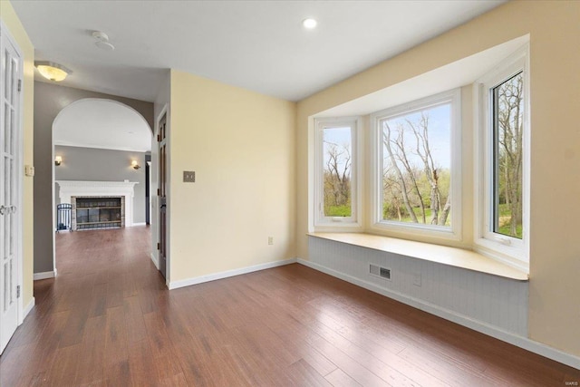 empty room with dark wood-style flooring, baseboards, a glass covered fireplace, and visible vents