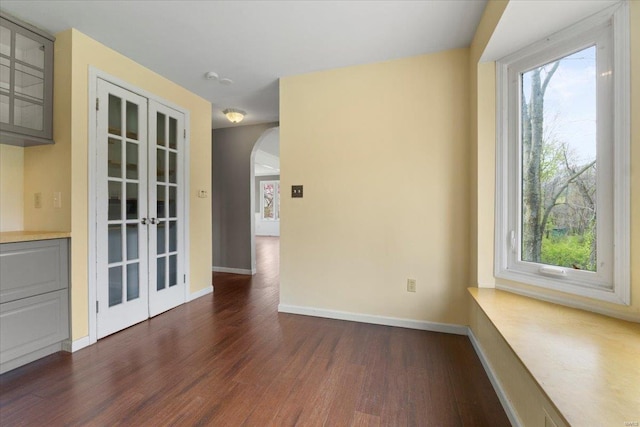 interior space with arched walkways, dark wood-style flooring, and baseboards
