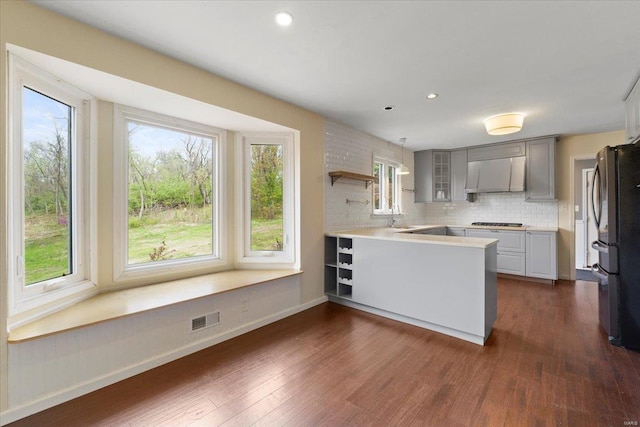 kitchen with freestanding refrigerator, a peninsula, gas stovetop, visible vents, and dark wood-style flooring