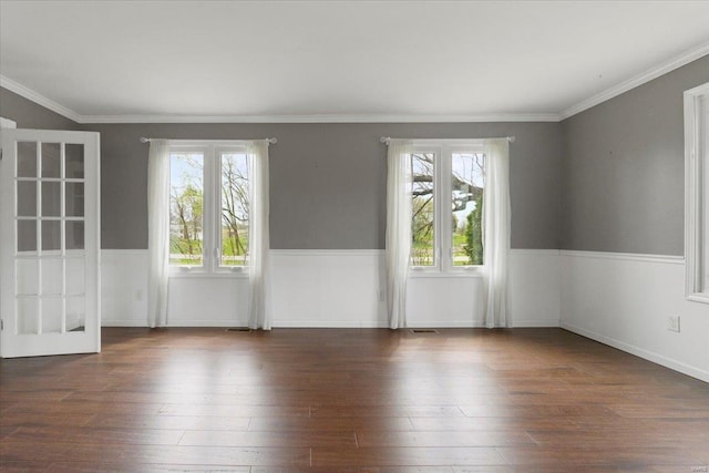 empty room featuring visible vents, crown molding, a wainscoted wall, and wood finished floors