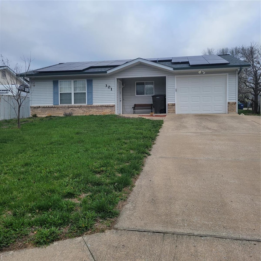 ranch-style house featuring an attached garage, brick siding, driveway, a front yard, and roof mounted solar panels