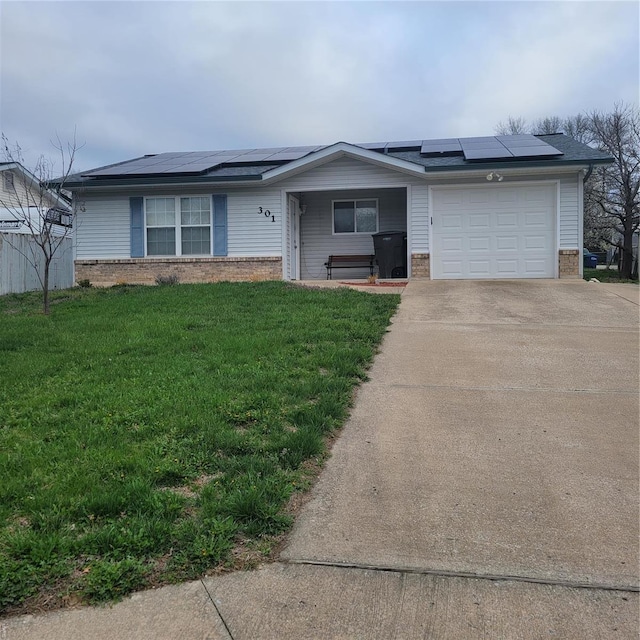 ranch-style house featuring an attached garage, brick siding, driveway, a front yard, and roof mounted solar panels