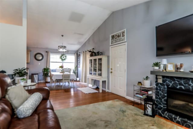 living room with vaulted ceiling, wood finished floors, and a stone fireplace