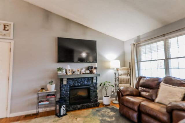 living area with lofted ceiling, baseboards, wood finished floors, and a stone fireplace