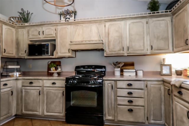 kitchen featuring light countertops, stainless steel microwave, vaulted ceiling, black range with gas stovetop, and light tile patterned floors