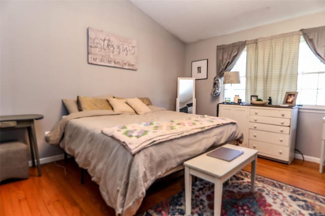 bedroom featuring lofted ceiling, baseboards, and light wood-style floors
