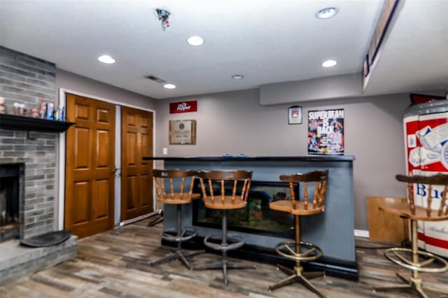 bar with a fireplace, a dry bar, wood finished floors, and recessed lighting
