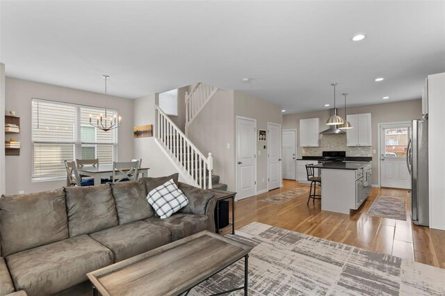 living room featuring light wood-type flooring, an inviting chandelier, stairs, and recessed lighting