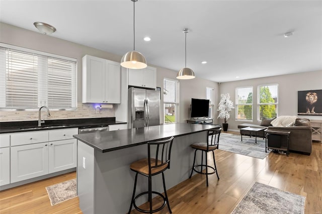 kitchen with a sink, light wood-style floors, dark countertops, appliances with stainless steel finishes, and open floor plan