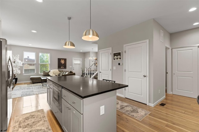kitchen featuring light wood-style floors, appliances with stainless steel finishes, dark countertops, baseboards, and open floor plan