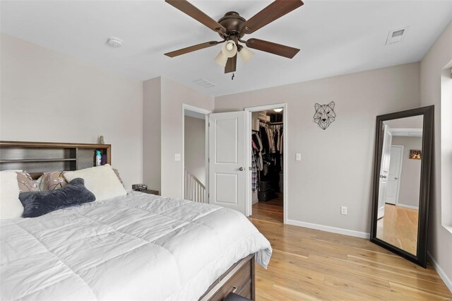 bedroom with visible vents, light wood-type flooring, a walk in closet, and baseboards