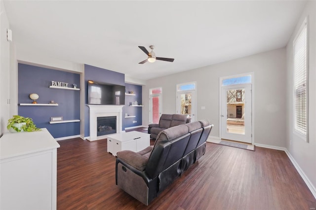 living room featuring a fireplace, dark wood-style flooring, ceiling fan, and built in features