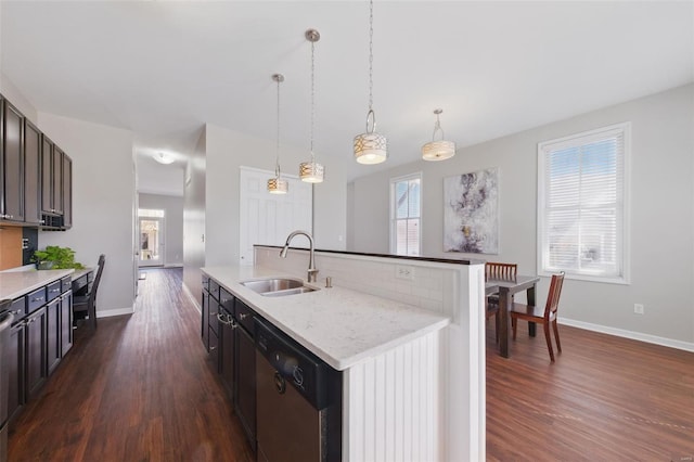 kitchen with an island with sink, a sink, stainless steel dishwasher, hanging light fixtures, and dark wood-style floors