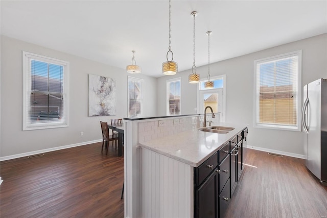 kitchen featuring freestanding refrigerator, a sink, dark wood-style floors, and an island with sink