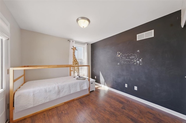 unfurnished bedroom with baseboards, visible vents, an accent wall, and wood finished floors