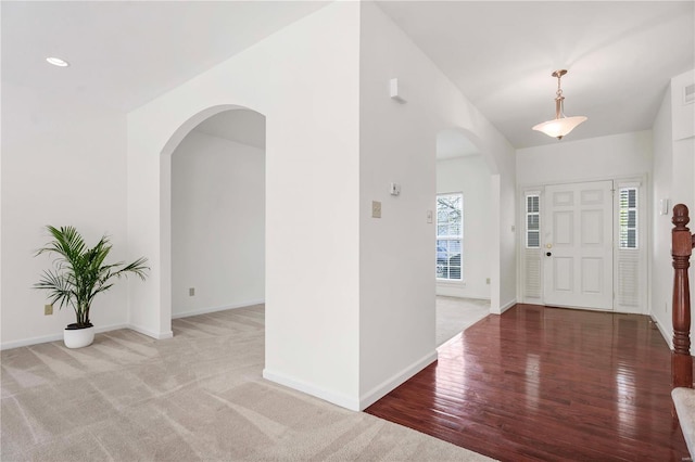 carpeted foyer entrance featuring wood finished floors, baseboards, visible vents, and arched walkways