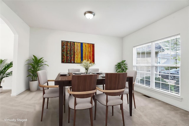 dining room with light colored carpet, visible vents, baseboards, and arched walkways