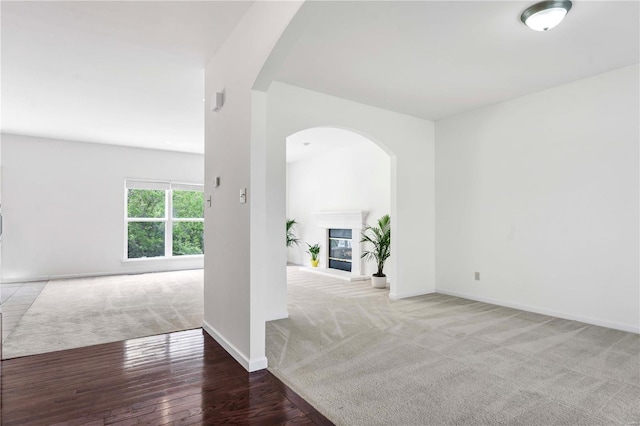 unfurnished room featuring a glass covered fireplace, arched walkways, carpet floors, and baseboards