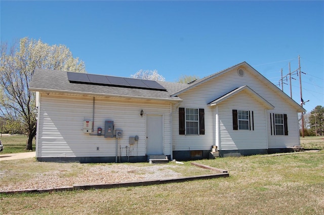 rear view of house featuring entry steps, roof with shingles, roof mounted solar panels, and a yard