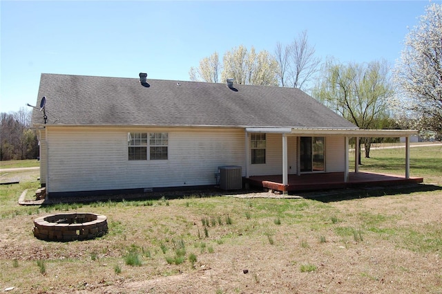 back of property featuring roof with shingles, a fire pit, central AC unit, and a yard