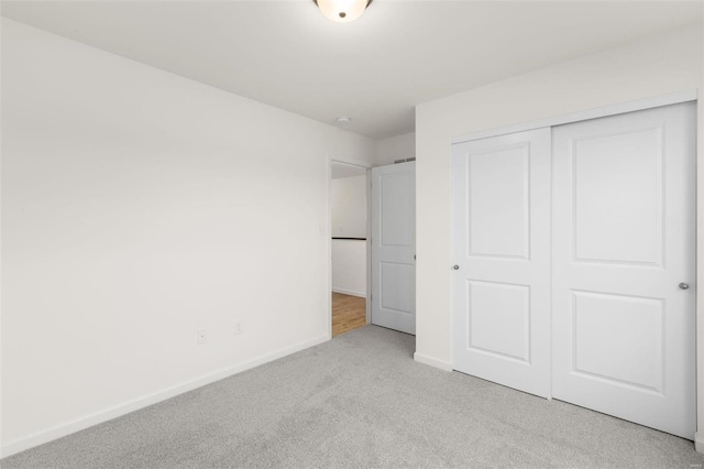 unfurnished bedroom with light carpet, baseboards, and a closet